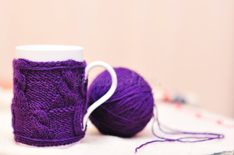O copo branco com violeta fez malha a camisola nele com a bola do fio foto de stock O copo branco com violeta fez malha a camisola nele com a bola do fio foto de stock