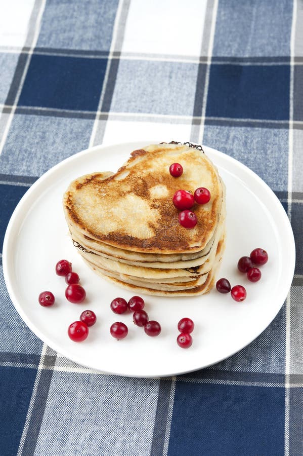 Heart shaped pancakes with cranberries on white porcelain plate. Morning celebration breakfast. Indoors closeup. Heart shaped pancakes with cranberries on white porcelain plate. Morning celebration breakfast. Indoors closeup.