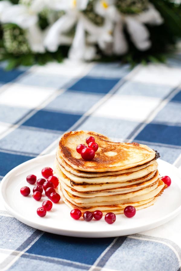 Heart shaped pancakes with cranberries on white porcelain plate. Celebration dessert with flowers on background. Indoors closeup. Heart shaped pancakes with cranberries on white porcelain plate. Celebration dessert with flowers on background. Indoors closeup.