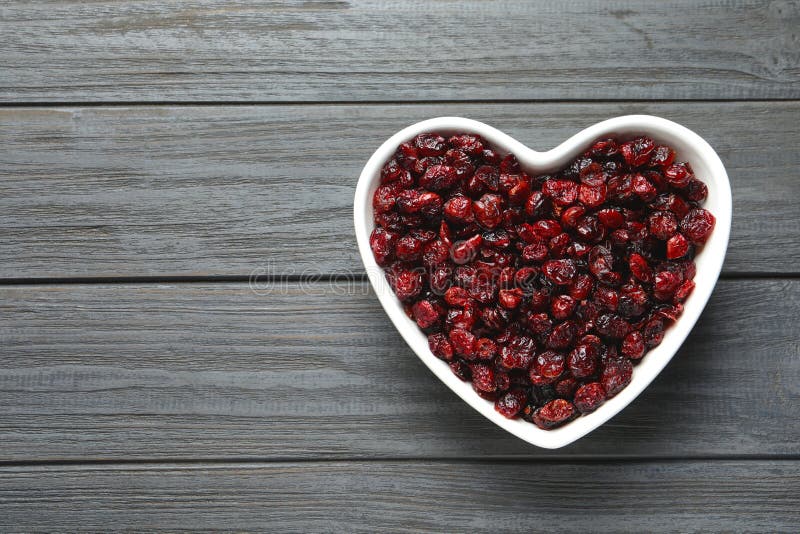 Heart shaped bowl with cranberries on wooden background, top view with space for text. Dried fruit as healthy snack. Heart shaped bowl with cranberries on wooden background, top view with space for text. Dried fruit as healthy snack