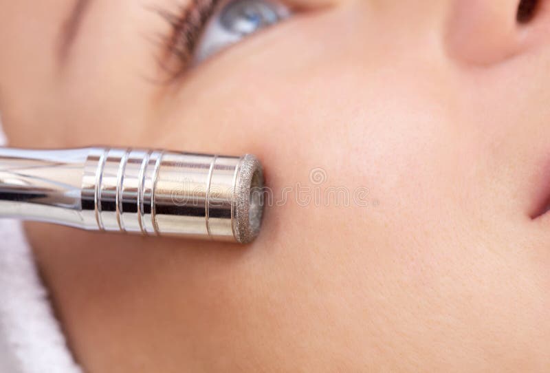 O cosmetologist faz o procedimento Microdermabrasion da pele facial de um bonito, jovem mulher em um salão de beleza imagem de stock O cosmetologist faz o procedimento Microdermabrasion da pele facial de um bonito, jovem mulher em um salão de beleza imagem de stock