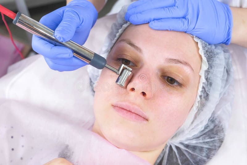 O Cosmetologist faz um procedimento micro-atual para a cara de uma jovem mulher Close-up da cara, vista dianteira fotografia de stock royalty free O Cosmetologist faz um procedimento micro-atual para a cara de uma jovem mulher Close-up da cara, vista dianteira fotografia de stock royalty free