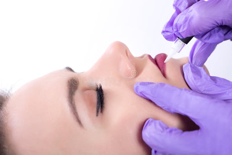 O Cosmetologist que aplica o permanent compõe nos bordos vermelhos imagem de stock royalty free O Cosmetologist que aplica o permanent compõe nos bordos vermelhos imagem de stock royalty free
