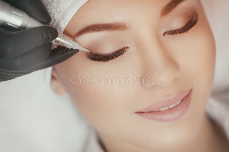 O Cosmetologist que faz o permanent compõe no salão de beleza foto de stock royalty free O Cosmetologist que faz o permanent compõe no salão de beleza foto de stock royalty free