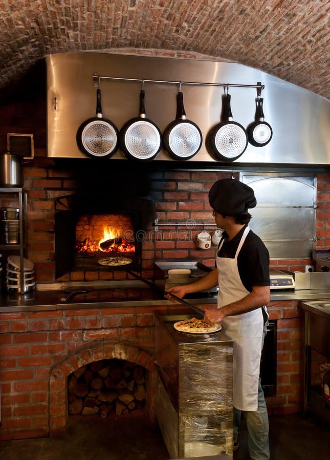 O cozinheiro chefe da pizza põr a pizza dentro do forno de madeira foto de stock O cozinheiro chefe da pizza põr a pizza dentro do forno de madeira foto de stock