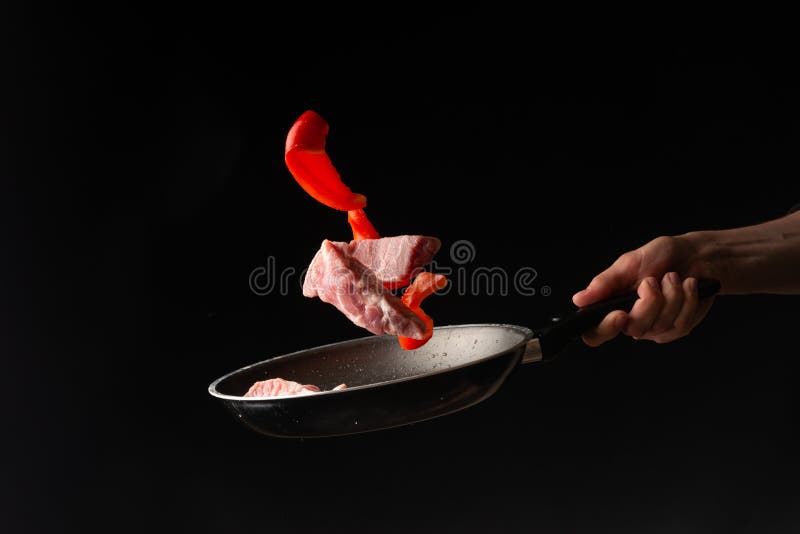 O cozinheiro chefe lan? a carne de porco ou o bife fresco com a pimenta doce, congelada no ar, em um fundo preto fotografia de stock royalty free O cozinheiro chefe lan? a carne de porco ou o bife fresco com a pimenta doce, congelada no ar, em um fundo preto fotografia de stock royalty free