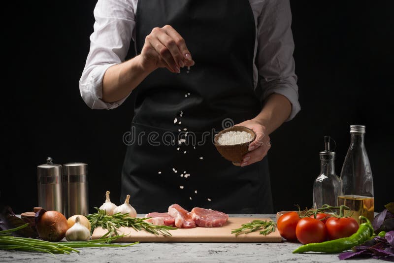 O cozinheiro chefe salga a bandeja da grade do bife Preparando a carne ou a carne de porco fresca Foto horizontal com um fundo pr fotografia de stock O cozinheiro chefe salga a bandeja da grade do bife Preparando a carne ou a carne de porco fresca Foto horizontal com um fundo pr fotografia de stock