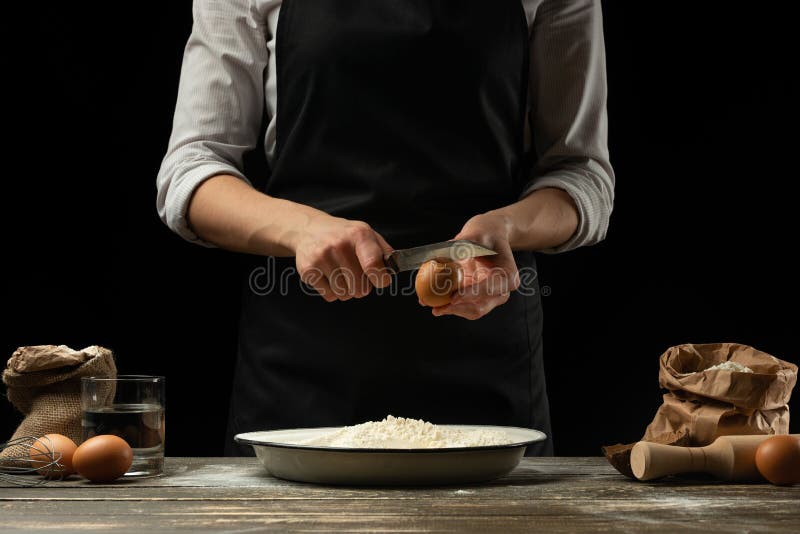 O cozinheiro chefe trabalha com massa, quebra o ovo e os chicotes, para a preparação do focaccia, da massa italiana, da pizza ou foto de stock O cozinheiro chefe trabalha com massa, quebra o ovo e os chicotes, para a preparação do focaccia, da massa italiana, da pizza ou foto de stock
