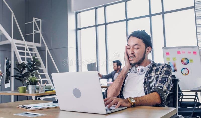 O criativo designer dá um tapa na cara quando está sonolento e trabalha duro com o laptop no escritório moderno conceito de estil imagens de stock O criativo designer dá um tapa na cara quando está sonolento e trabalha duro com o laptop no escritório moderno conceito de estil imagens de stock
