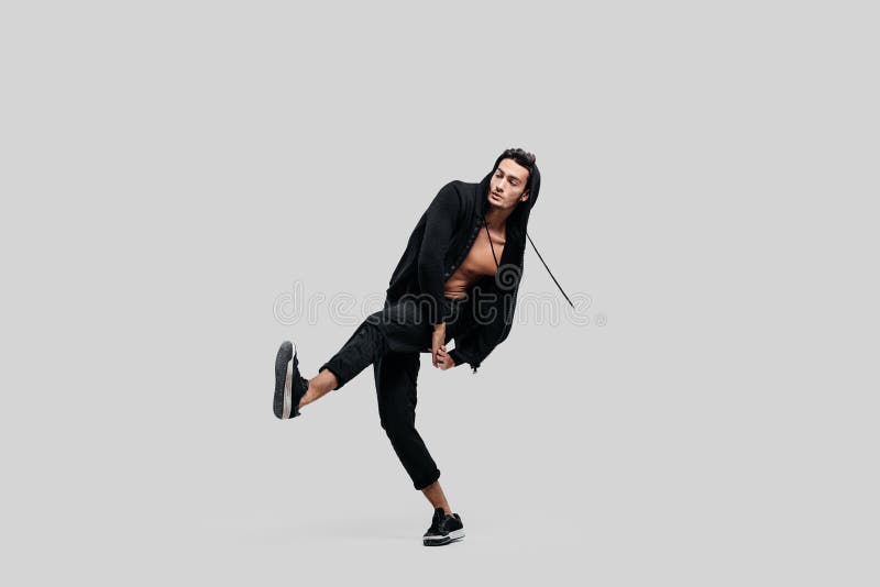 O dançarino novo considerável vestido em calças pretas, uma camiseta em um torso despido levanta um pé acima ao dançar a dança da fotos de stock royalty free O dançarino novo considerável vestido em calças pretas, uma camiseta em um torso despido levanta um pé acima ao dançar a dança da fotos de stock royalty free