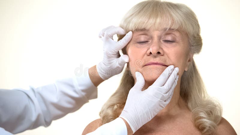 O dermatologista que examina a pele paciente f?mea idosa, enruga a remo??o, beleza fotografia de stock royalty free O dermatologista que examina a pele paciente f?mea idosa, enruga a remo??o, beleza fotografia de stock royalty free