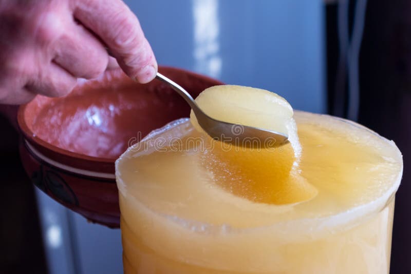 O deslocamento do mel de um recipiente maior em uma bacia foto de stock O deslocamento do mel de um recipiente maior em uma bacia foto de stock