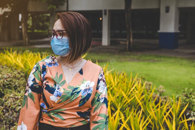 O doamnă cu părul scurt care poartă o mască chirurgicală și o bluză tropicală portocalie care se plimbă pe piața mall-ului stock photography