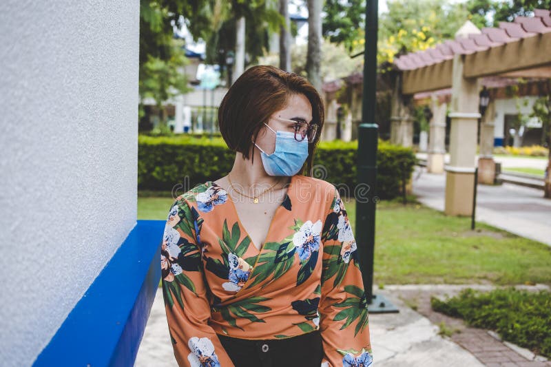 O doamnă cu părul scurt care poartă o mască chirurgicală și o bluză tropicală portocalie care se plimbă într-un mall royalty free stock images