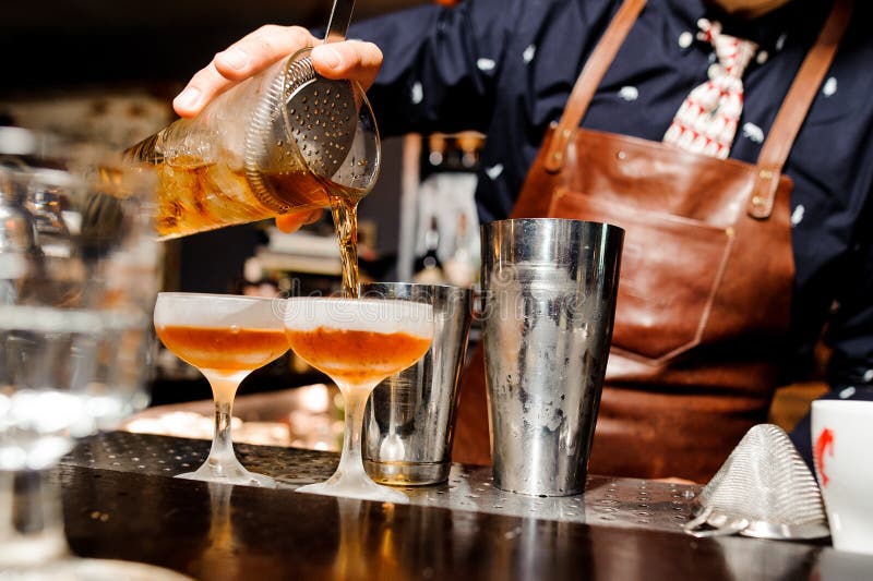 O empregado de bar termina a preparação de dois cocktail alcoólicos usando o equipamento da barra fotografia de stock O empregado de bar termina a preparação de dois cocktail alcoólicos usando o equipamento da barra fotografia de stock