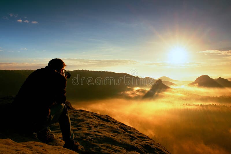 O entusiasta feliz da foto está apreciando o milagre fantástico da natureza no penhasco na rocha Fole sonhador da paisagem do fog fotografia de stock O entusiasta feliz da foto está apreciando o milagre fantástico da natureza no penhasco na rocha Fole sonhador da paisagem do fog fotografia de stock