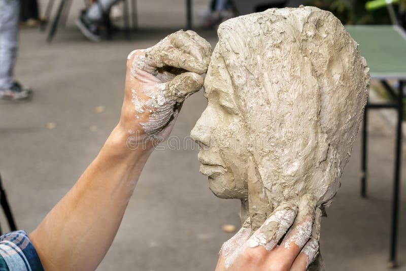 o escultor cria um busto e põe sua argila das mãos sobre o esqueleto da escultura