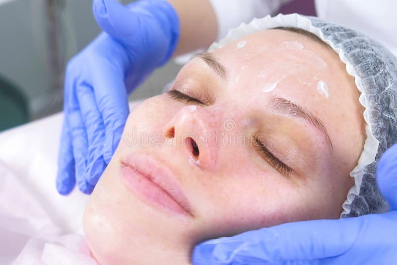 O esteticista põe o creme sobre a cara da mulher Tratamento facial do Cosmetologist Close-up fotografia de stock royalty free O esteticista põe o creme sobre a cara da mulher Tratamento facial do Cosmetologist Close-up fotografia de stock royalty free