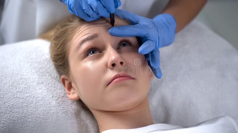 O esteticista que marca a testa profunda enruga-se na cara dos clientes, procedimentos da beleza fotos de stock royalty free O esteticista que marca a testa profunda enruga-se na cara dos clientes, procedimentos da beleza fotos de stock royalty free