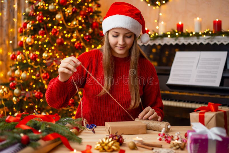 O fată veselă cu pălărie roșie și un pulover strălucitor care împachetează cadouri de Crăciun stock photo