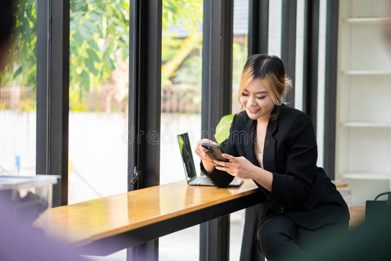O femeie asiatică frumoasă care vorbește pe telefonul mobil și se joacă cu un notebook care zâmbește în timp ce stă la birou. part stock images