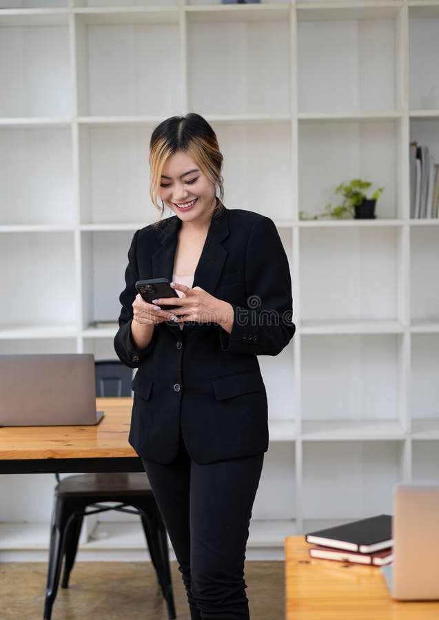 O femeie asiatică vorbește pe un telefon mobil sau smartphone în timp ce lucrează pe un calculator la biroul său. royalty free stock photos