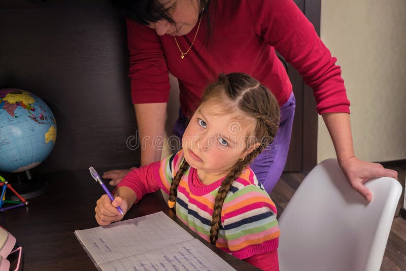 O fetiță nu vrea să învețe lecții. trist copil este obosit de teme școlare. mama o ajută pe fiica ei să-și facă temele. i cu stock image
