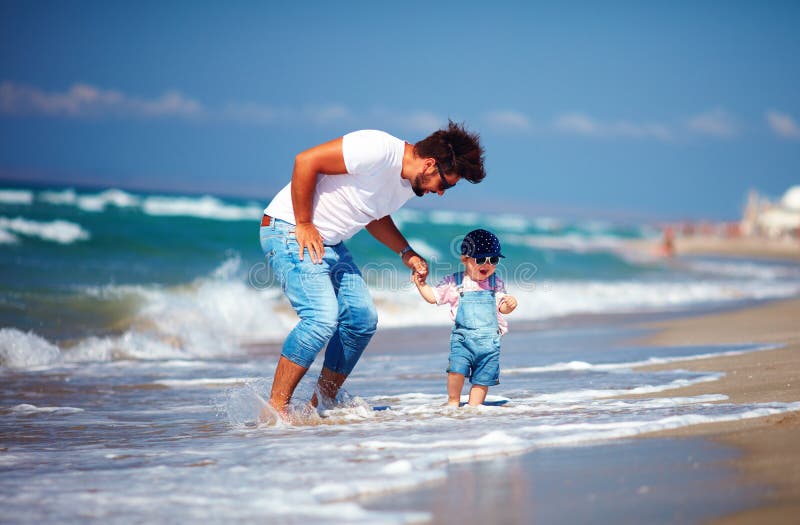 O filho brincalhão do pai e da criança que tem o divertimento que salta no mar acena durante férias de verão, jogos da atividade