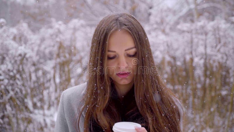 O fim acima da mulher triste bonita nova com o copo descartável do café ou de chá está sentando-se em um banco fora em um parque