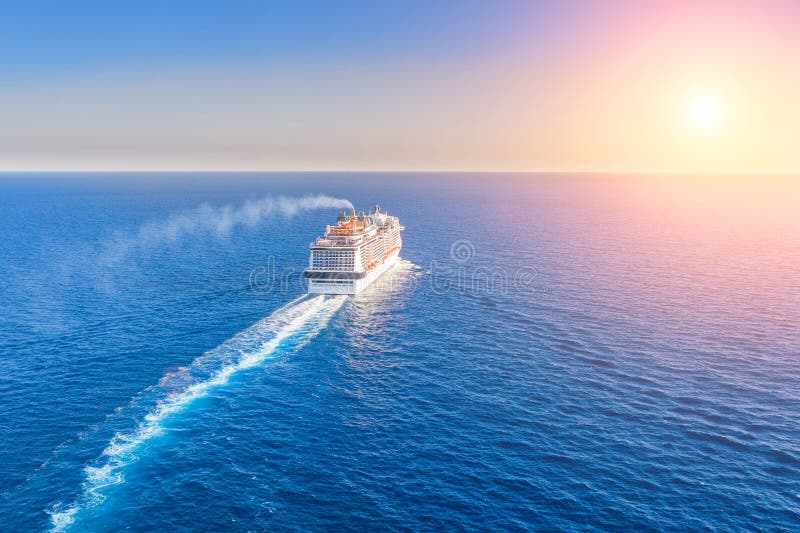 O forro do navio de cruzeiros entra no horizonte o mar azul que deixa uma pena na superfície do seascape da água durante o por do