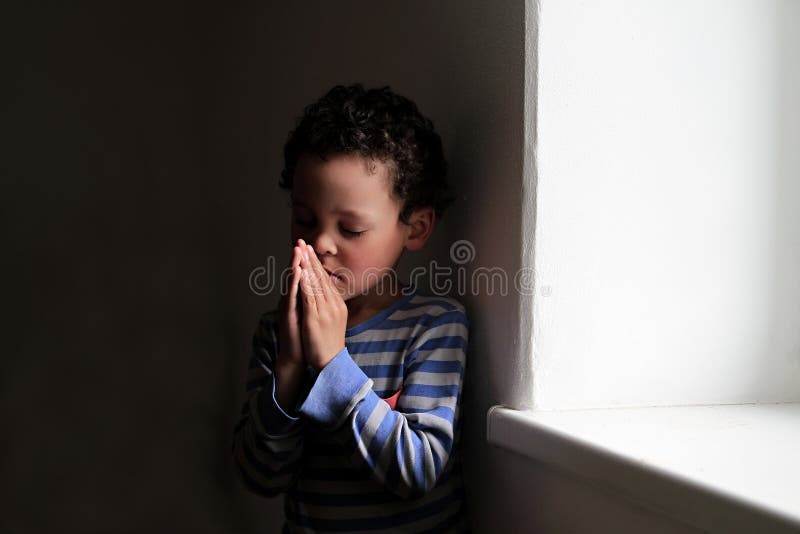 O garotinho rezando para Deus com as mãos juntas.