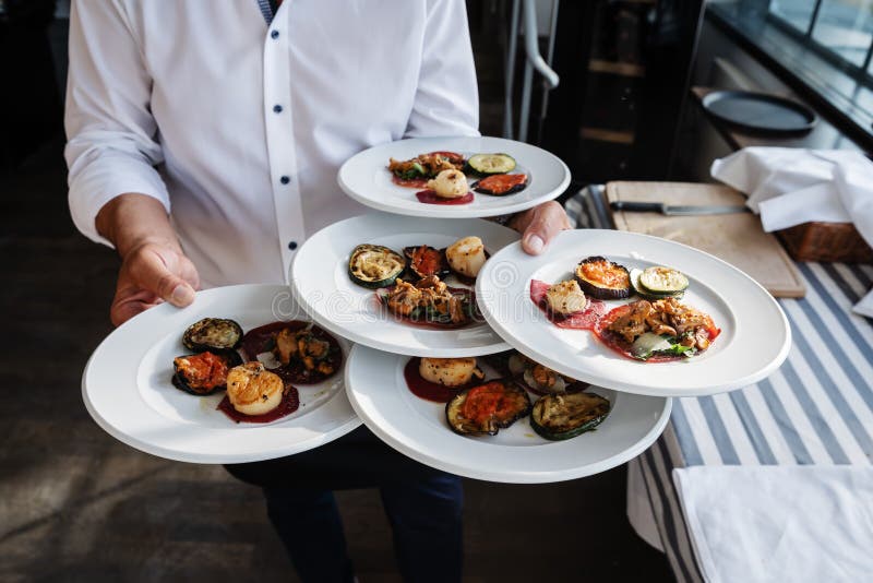 O garçom serve antipasti italianos em um restaurante exterior fotografia de stock O garçom serve antipasti italianos em um restaurante exterior fotografia de stock