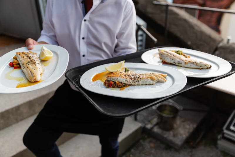 O garçom serve pratos com peixes imagens de stock O garçom serve pratos com peixes imagens de stock