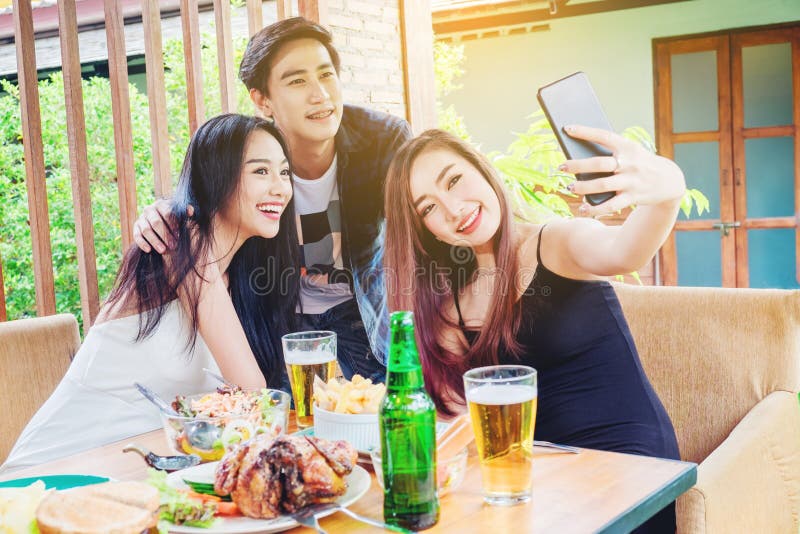 O grupo de amigos está tomando o selfie e comendo o alimento seja enj feliz imagem de stock O grupo de amigos está tomando o selfie e comendo o alimento seja enj feliz imagem de stock