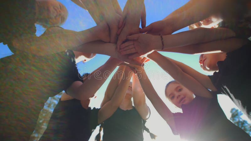 O grupo de crianças da escola executa o cumprimento inspirador dos esportes com as mãos no campo de jogos do futebol da jarda no