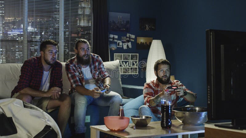 O grupo de homens joga o videogame junto na noite fotos de stock O grupo de homens joga o videogame junto na noite fotos de stock