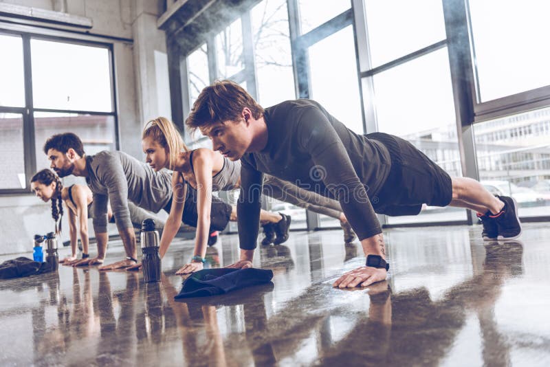 O grupo de jovens atléticos em fazer do sportswear empurra levanta ou prancha no gym imagens de stock royalty free O grupo de jovens atléticos em fazer do sportswear empurra levanta ou prancha no gym imagens de stock royalty free
