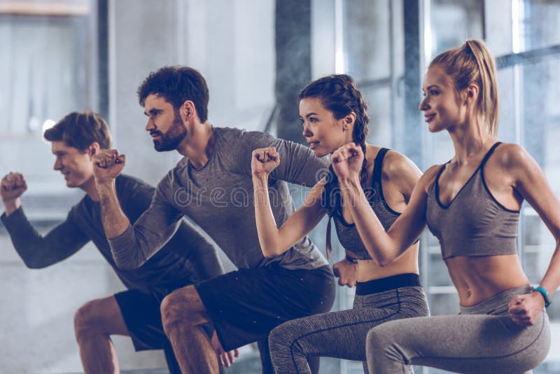 O grupo de jovens atléticos em fazer do sportswear investe contra o exercício no gym fotografia de stock O grupo de jovens atléticos em fazer do sportswear investe contra o exercício no gym fotografia de stock