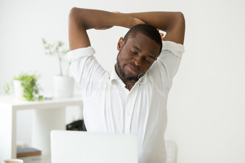 O homem afro-americano que estica fazendo o escritório exercita em sedent