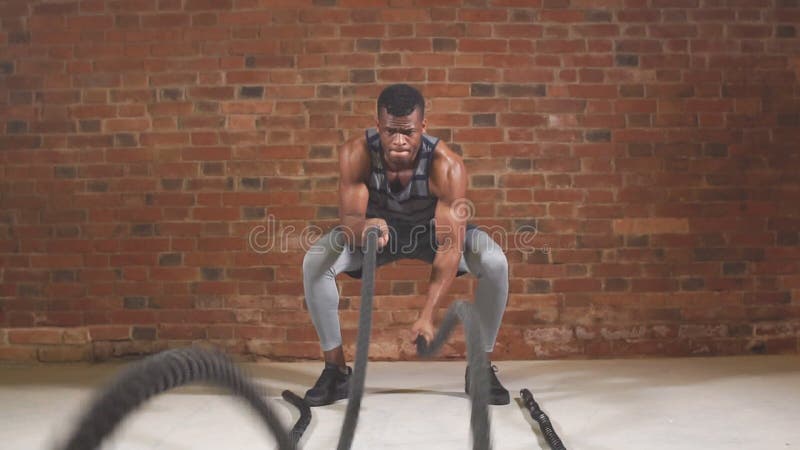 O homem chested desencapado muscular considerável do gym está fazendo o exercício da corda da batalha Movimento lento