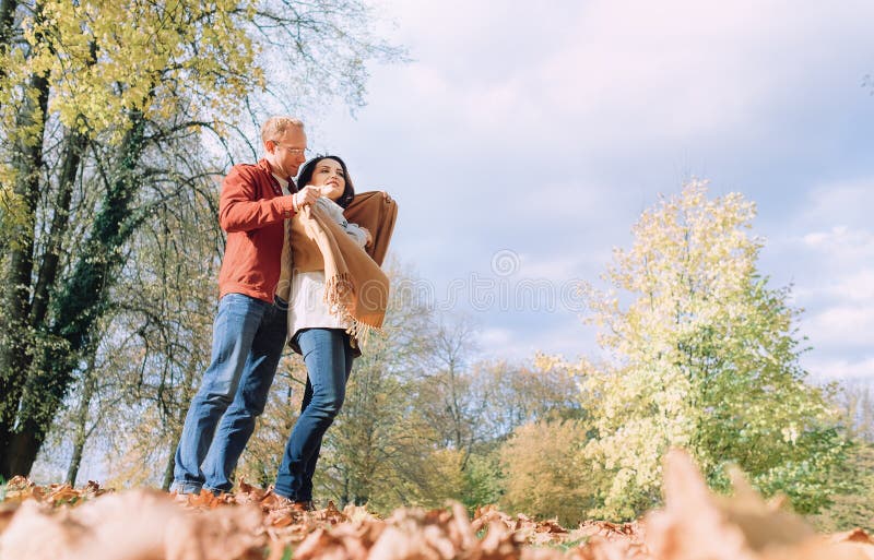 O homem cobre seus ombros da esposa com o xaile morno no parque do outono fotos de stock royalty free O homem cobre seus ombros da esposa com o xaile morno no parque do outono fotos de stock royalty free