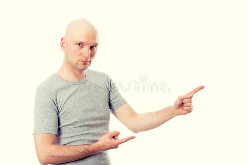 O homem com cabeça calva na camisa cinzenta está apontando ao lado fotografia de stock O homem com cabeça calva na camisa cinzenta está apontando ao lado fotografia de stock