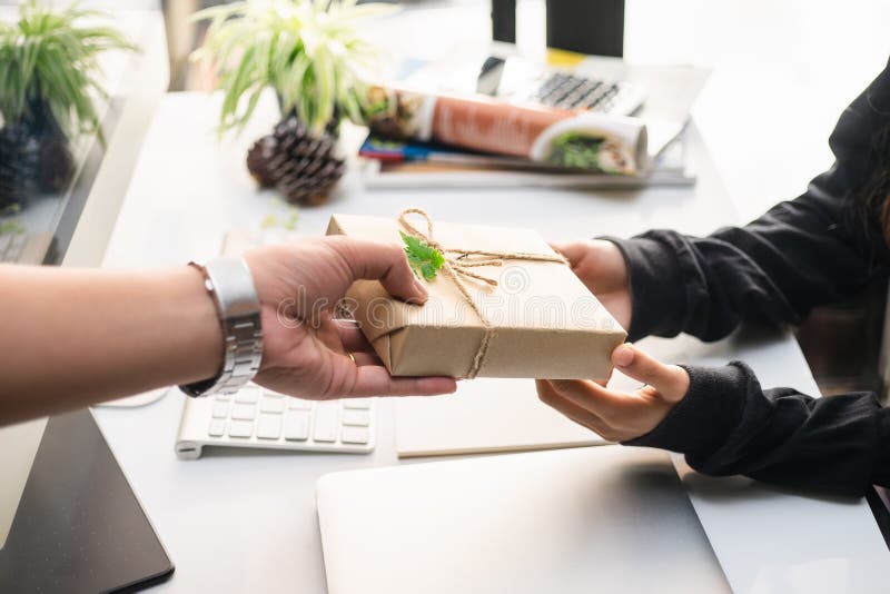 O homem da mão que guarda um papel envolvido caixa de presente do ofício com a fita para a mulher de negócio bonita, sente da fel fotos de stock royalty free O homem da mão que guarda um papel envolvido caixa de presente do ofício com a fita para a mulher de negócio bonita, sente da fel fotos de stock royalty free