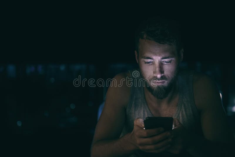 O homem da noite escura olhando para a tela do celular mandando mensagens tarde da noite acordado na insônia da cama ou fora da c imagem de stock O homem da noite escura olhando para a tela do celular mandando mensagens tarde da noite acordado na insônia da cama ou fora da c imagem de stock