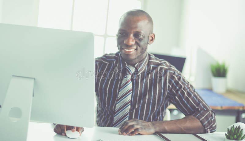 O homem de neg?cios afro-americano consider?vel no terno cl?ssico est? usando um port?til e est? sorrindo ao trabalhar no escrit? foto de stock royalty free O homem de neg?cios afro-americano consider?vel no terno cl?ssico est? usando um port?til e est? sorrindo ao trabalhar no escrit? foto de stock royalty free