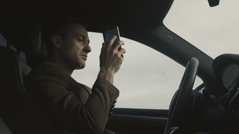 O homem de negócio fala pelo telefone que senta-se no carro