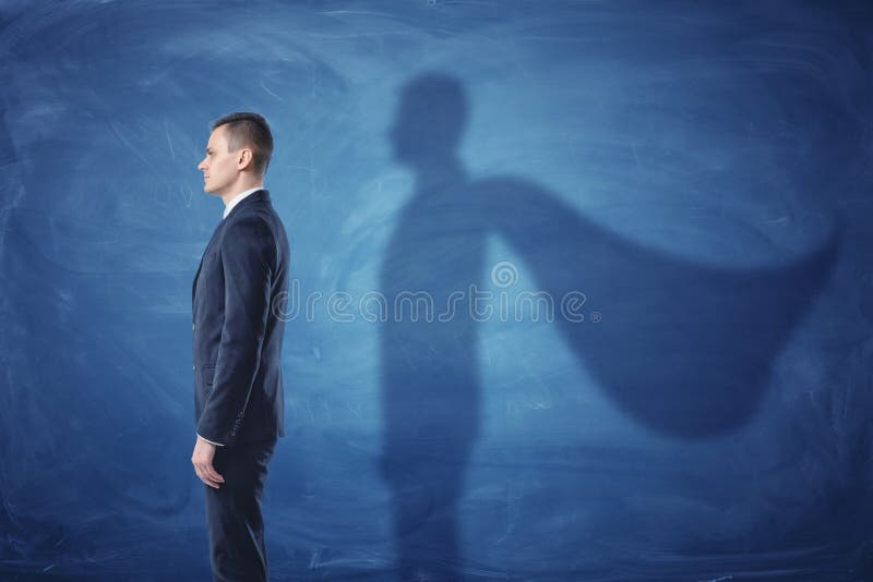 O homem de negócios está estando no perfil que molda uma sombra do cabo do ` s do superman no fundo azul do quadro