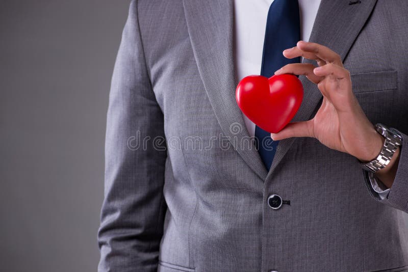 O homem de negócios que guarda o coração vermelho no conceito do amor fotografia de stock royalty free O homem de negócios que guarda o coração vermelho no conceito do amor fotografia de stock royalty free