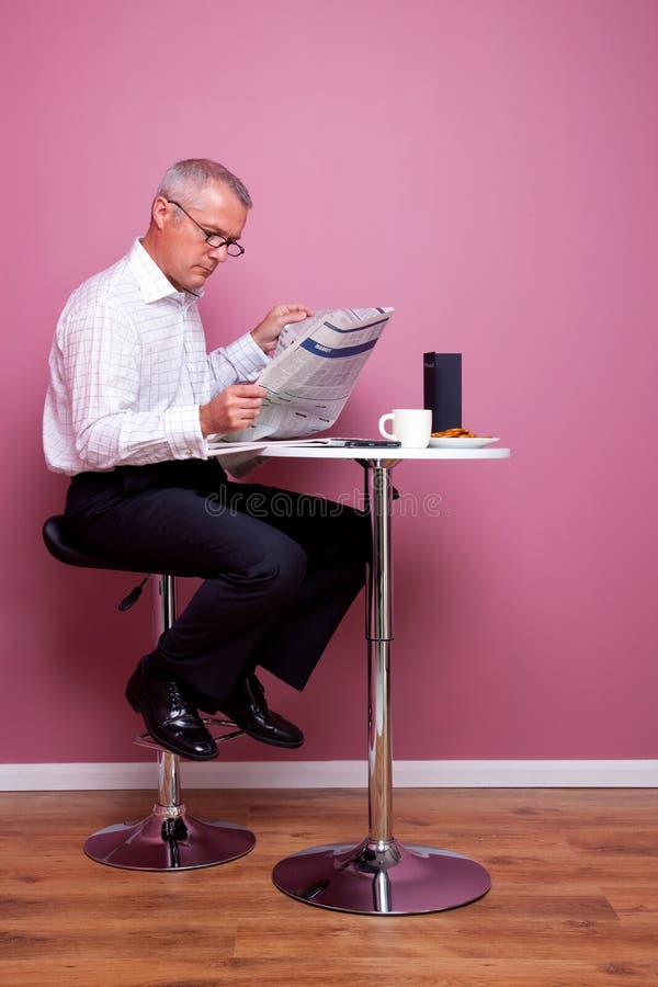 O homem de negócios que lê um jornal sentou-se em um café