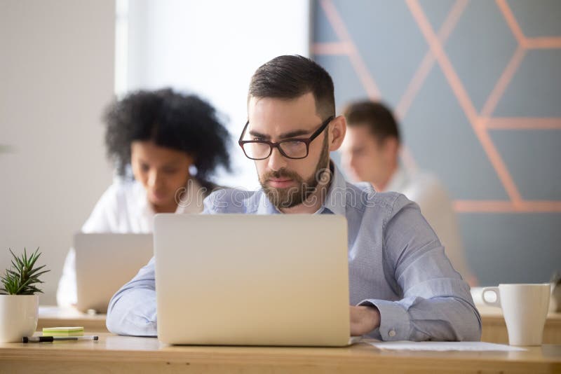 O homem de negócios sério centrou-se sobre o trabalho em linha do computador em coworking imagem de stock royalty free O homem de negócios sério centrou-se sobre o trabalho em linha do computador em coworking imagem de stock royalty free